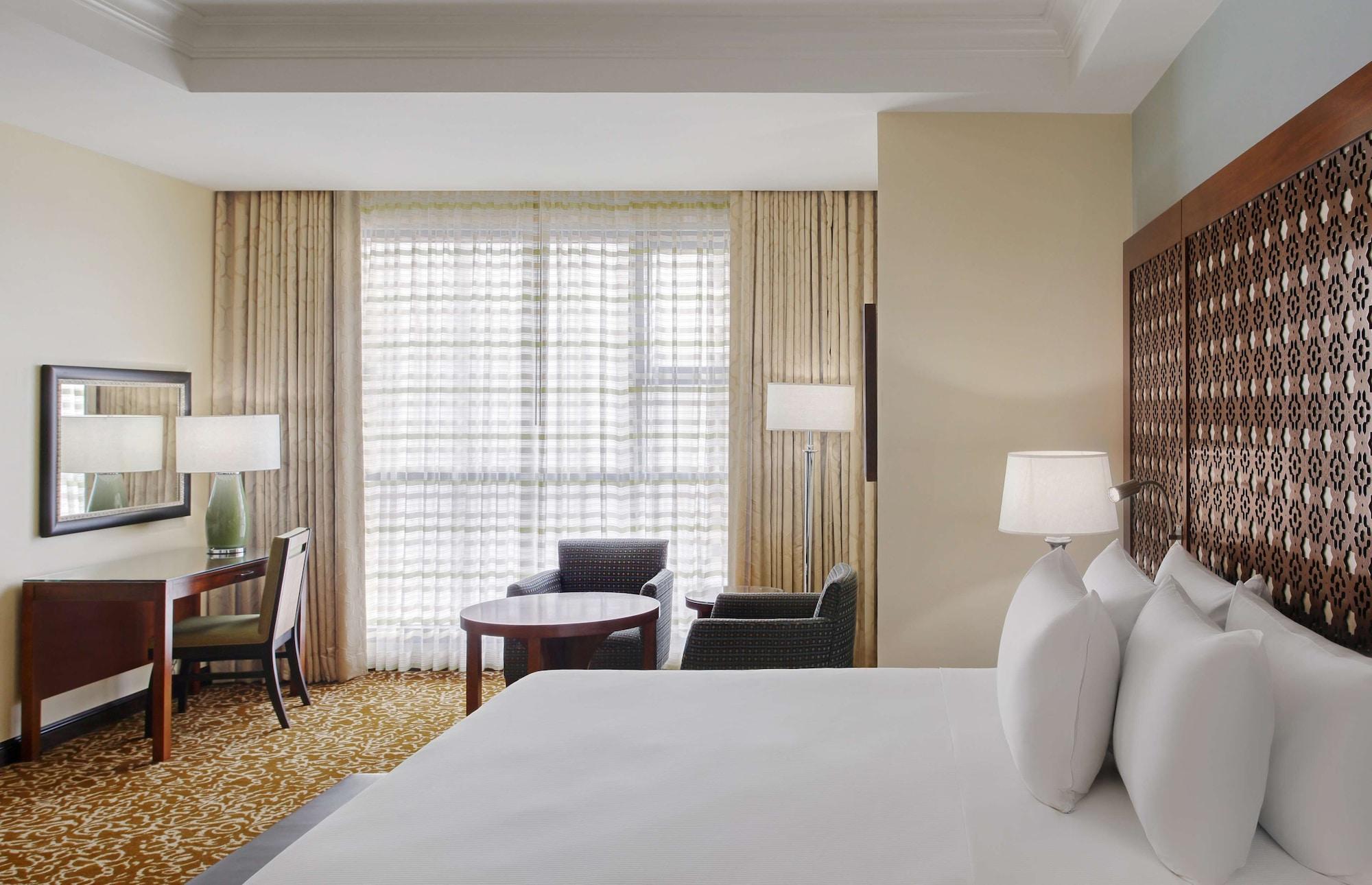 Hilton Suites Jabal Omar Makkah Mekka Exterior foto The photo shows a hotel room with a modern design. In the foreground, there is a large bed with several white pillows. In the background, you can see a window with sheer curtains that allow natural light to fill the room. There are two armchairs and 