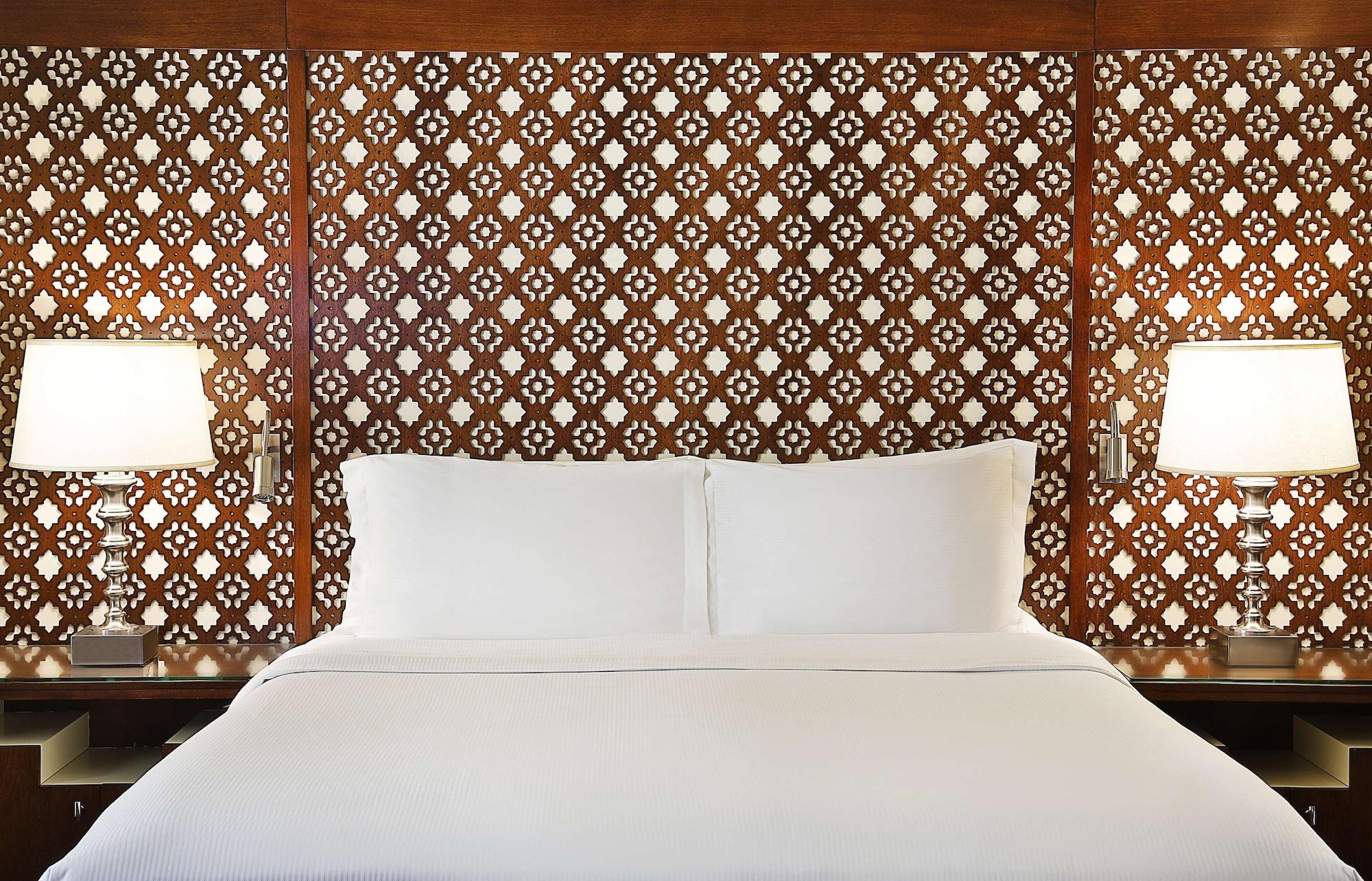 Hilton Suites Jabal Omar Makkah Mekka Exterior foto The image shows a well-appointed bedroom setting with a large, neatly made bed featuring a white duvet and pillows. The headboard is constructed from intricately designed wood, showcasing a geometric pattern that adds an elegant touch to the room. On
