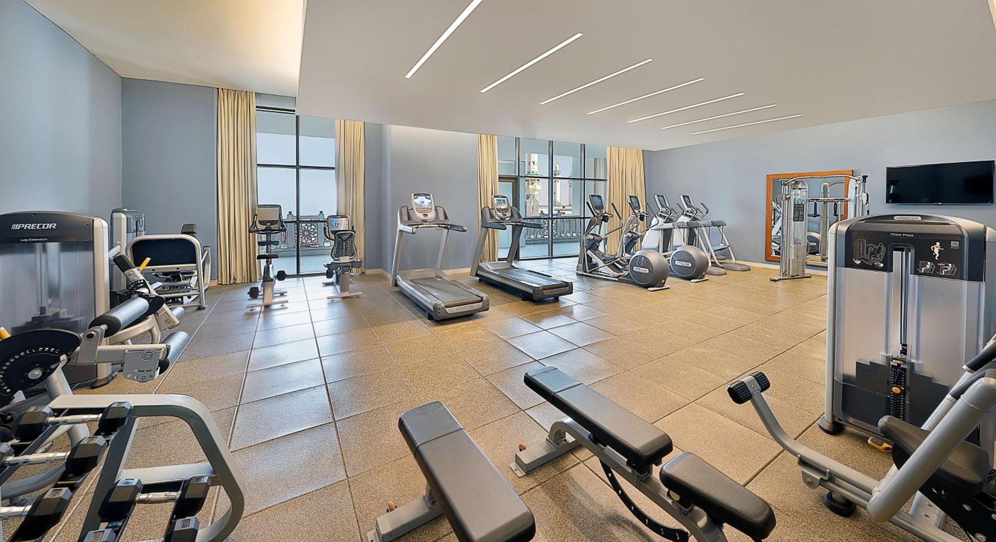Hilton Suites Jabal Omar Makkah Mekka Exterior foto The photo shows a modern gym or fitness room. It features several pieces of exercise equipment, including treadmills, elliptical machines, and weight benches. The space has large windows that allow natural light to fill the room. The walls are painte