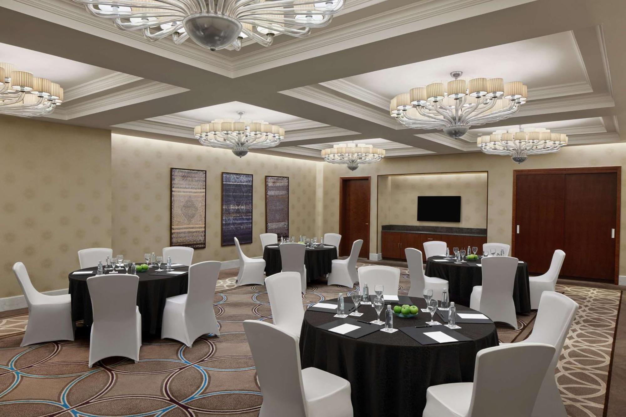 Hilton Suites Jabal Omar Makkah Mekka Exterior foto The photo shows an elegant banquet or conference room. It features several round tables covered with black tablecloths, each set with glassware, plates, and small green centerpieces. The chairs are white and neatly arranged around the tables. The roo