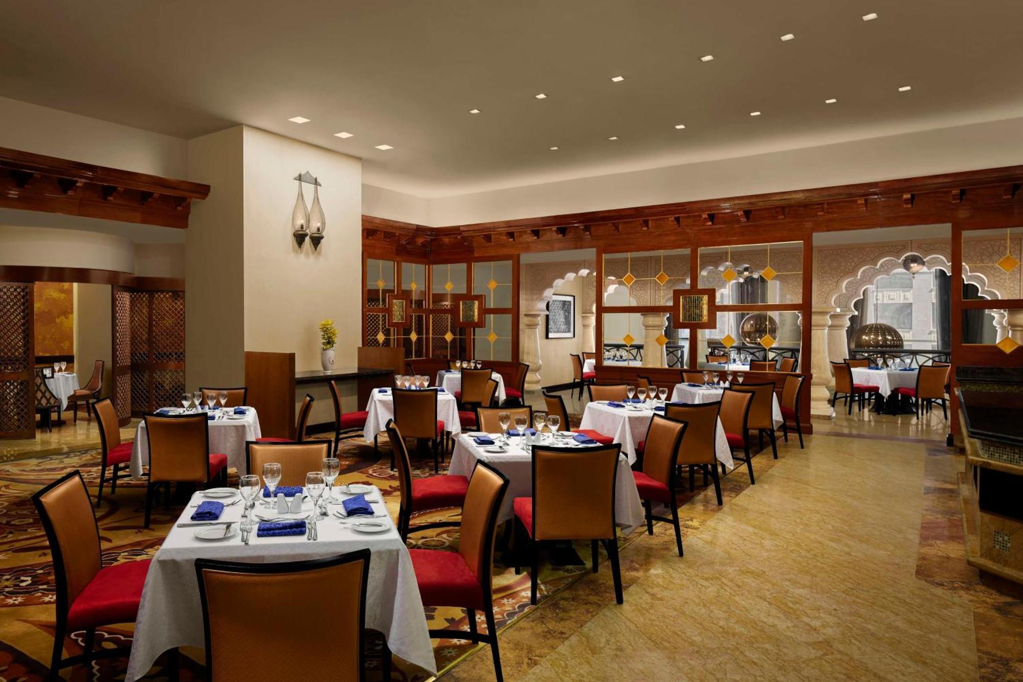 Hilton Suites Jabal Omar Makkah Mekka Exterior foto The photo depicts a restaurant interior characterized by elegant decor. The space features several tables set with white tablecloths, plates, cutlery, and blue napkins. The chairs are orange with a contemporary design, and there seems to be a well-li