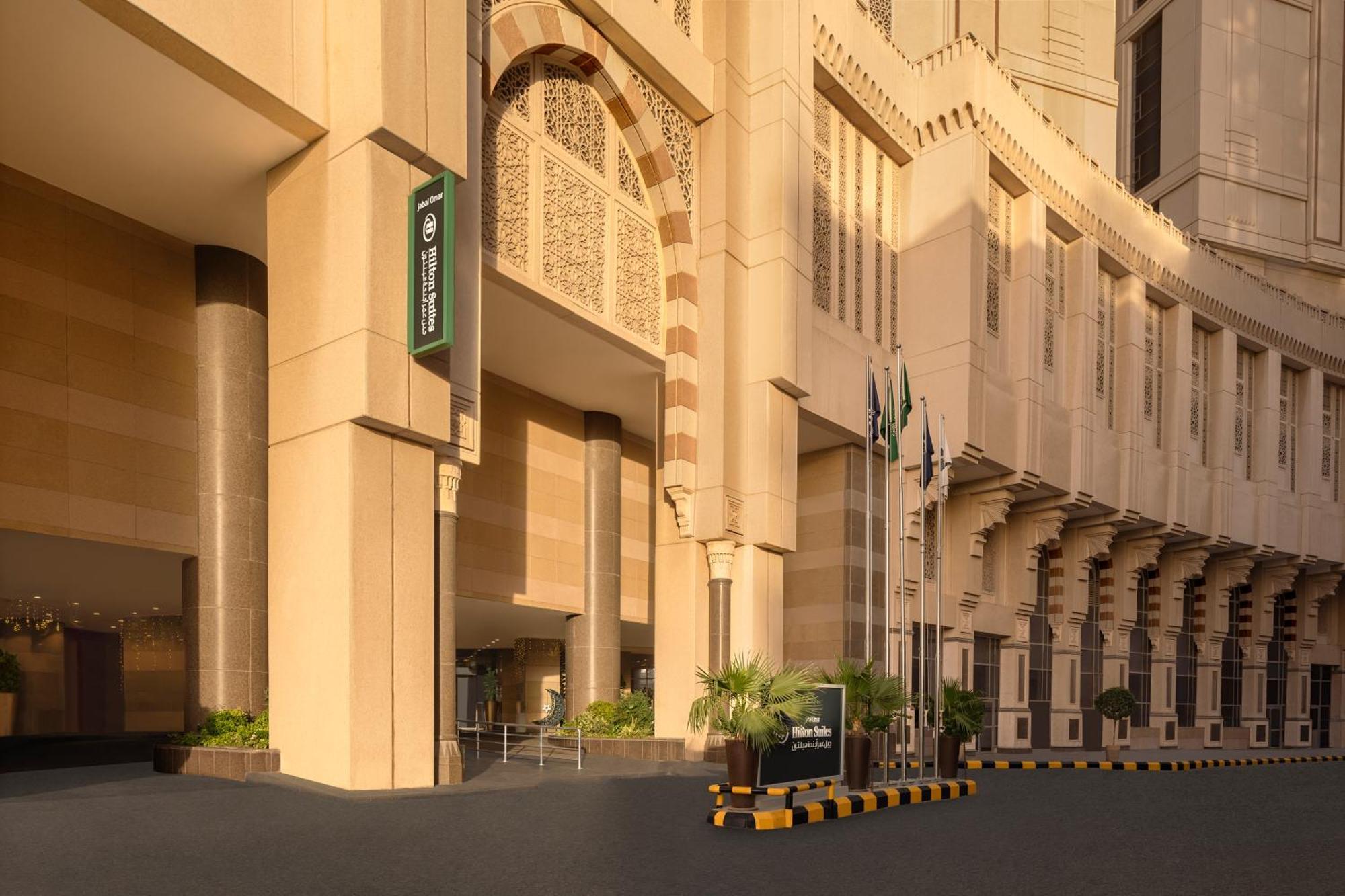 Hilton Suites Jabal Omar Makkah Mekka Exterior foto The photo shows a modern building with a distinctive architectural style, featuring large, light-colored stone facades. The entrance is prominent, with a wide, inviting pathway leading up to it. To the left, there is a sign that appears to indicate t