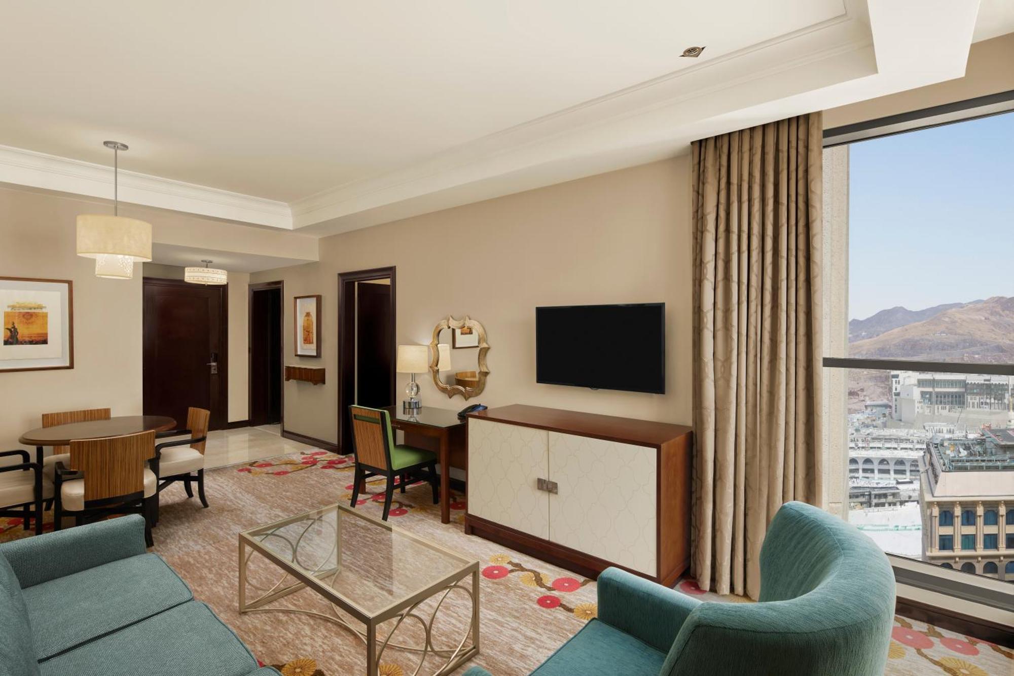 Hilton Suites Jabal Omar Makkah Mekka Exterior foto The photo depicts a modern hotel room or suite. It features a spacious living area with a comfortable sofa and armchairs. A glass coffee table sits in the center, adding to the inviting atmosphere. There’s a flat-screen TV mounted on the wall opposit